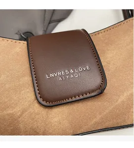 Detail of khaki twill fabric and brown leather flap with embossed logo on handbag