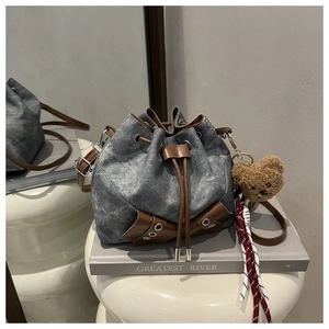 Detail of drawstring denim bucket bag with brown trim and cute teddy bear charm accessory