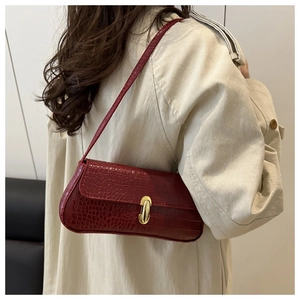 Detail of dark red crocodile embossed shoulder bag with gold metal buckle on trench coat