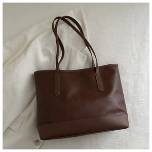 Detail of a large dark brown tote bag on a white textured bedsheet with a corduroy shirt