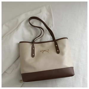 Close-up of minimalist tote bag featuring cream and brown patchwork with metal bow detail