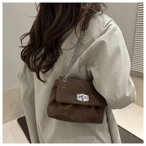 Detail of a brown suede shoulder bag with a sparkling diamond-encrusted buckle and silver chain