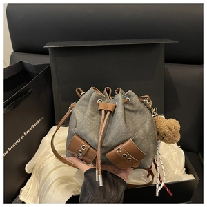 Close-up of drawstring denim bucket bag with leather accents and plush bear charm detail