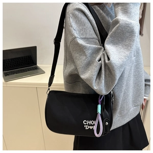 Détail du sac demi-lune en nylon noir avec broderie de lettres et pendentif coloré chic