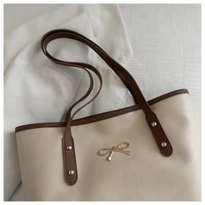 Close-up of minimalist cream tote bag with contrast brown trim and golden bow detail