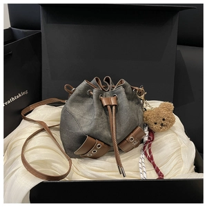 Detail of drawstring bucket bag in grey denim with leather trim and bear charm