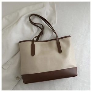 Flat lay of a beige and brown PU leather tote bag on white textured bedding