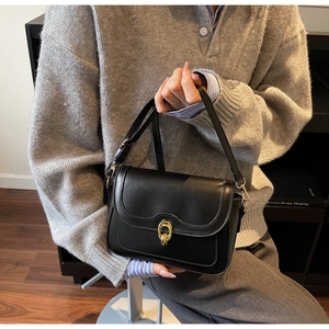 Close-up of black crossbody bag with gold buckle and scalloped flap on grey knit
