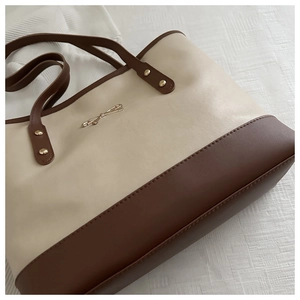 Close-up of minimalist cream and brown tote bag with golden bow hardware on white fabric