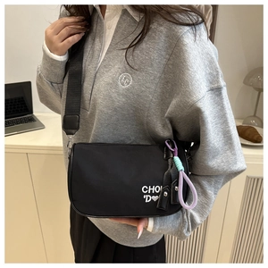 Détail du sac bandoulière en nylon noir avec broderie et breloque en nœud coloré