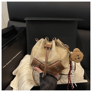 Detailed view of canvas drawstring bucket bag with leather trim and teddy bear charm