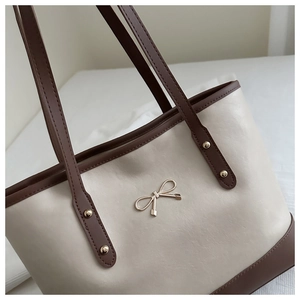 Close-up of contrast color tote bag featuring golden bow metal hardware and smooth texture