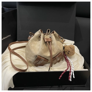 Detail of drawstring bucket bag with leather accents and bear charm on silk fabric