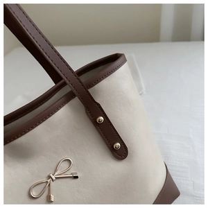 Detail of minimalist tote bag showing leather texture, stitching, and gold bow logo