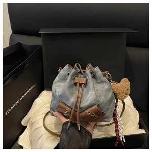 Detail of vintage denim drawstring bucket bag with leather trim and bear charm