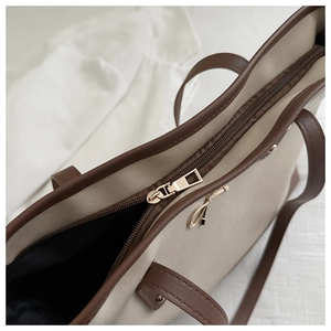 Detail of beige and brown tote bag showing gold bow hardware and zipper closure