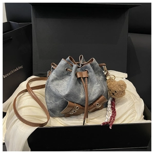 Close-up of denim bucket bag with brown leather accents and bear charm in a gift box
