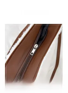 Detail view of smooth metal zipper closure on a brown textured leather and white plush bag