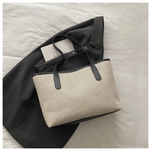 Detail der cremeweißen Canvas-Tasche mit schwarzem Lederbesatz auf dezentem Stoffhintergrund