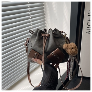 Detail of grey canvas drawstring bucket bag with brown leather trim and bear charm