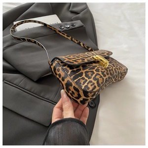 Detailed view of leopard print underarm bag with gold metal buckle on grey fabric