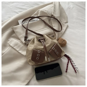 Detail of khaki canvas bucket bag with adjustable strap and decorative bear charm