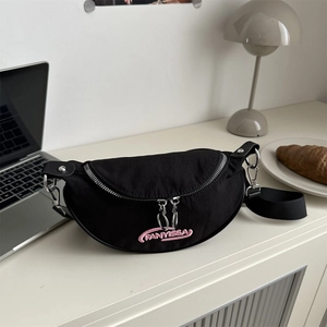 Sac bandoulière demi-lune noir avec broderie rose sur un bureau au style minimaliste
