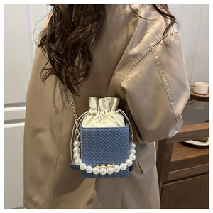 Detail view of blue woven square bag featuring pearl handle and gold chain strap on model