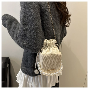 Detail of cream woven bucket bag with large pearl handle and gold chain strap shown on model