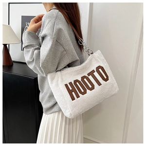 Detail of white plush tote bag with brown HOOTO lettering and leather chain strap