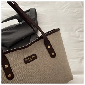Detail der beige gewebten Tragetasche mit braunem Lederbesatz und goldenem Logo
