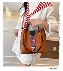 Detail of a brown leather handbag with colorful woven pattern and black round handles