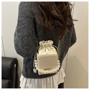 Detail of cream woven bucket bag with elegant pearl handle and gold chain strap