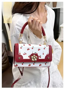 Detailed view of white leather handbag with cherry prints and a golden floral lock