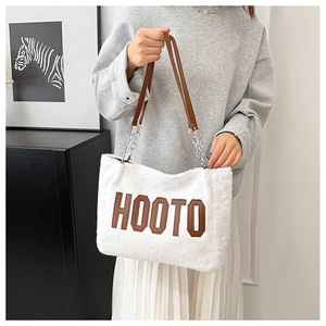Detail of white plush tote bag with brown HOOTO letters and leather chain strap