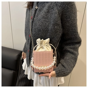 Close-up of pink woven crossbody bag with large pearl handle and silk drawstring bag