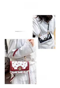 Close-up of white leather handbag with red cherry pattern and golden flower clasp