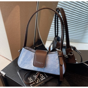 Close-up of denim baguette bag with brown leather trim and metallic brand lock buckle