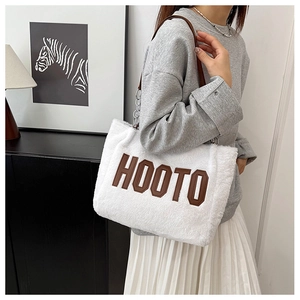 Detail of white plush tote bag with brown HOOTO embroidery and chain strap shoulder wear