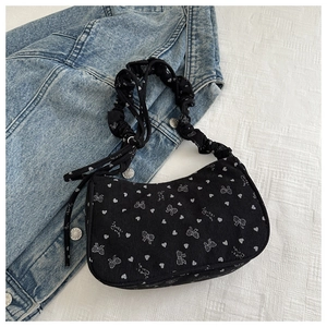 Close-up of black corduroy shoulder bag with white heart and bow prints and ruffled strap