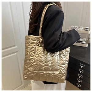 Detail of gold quilted tote bag with padded shoulder strap and knot design shown on model