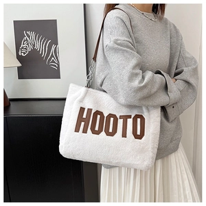 Close-up of white plush tote bag with brown HOOTO lettering and metal chain strap