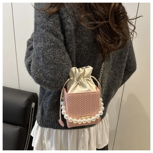 Rear view of pink woven crossbody bag with pearl handle and golden chain on model
