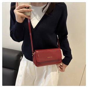Detail of red patent leather crossbody bag with gold lettering and slim shoulder strap