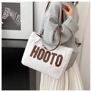Close-up of white plush tote bag with brown leather strap and HOOTO letter applique