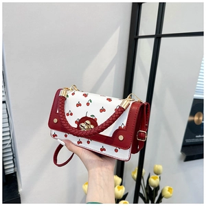 Detailed view of the woven red handle and cherry pattern on the white crossbody bag