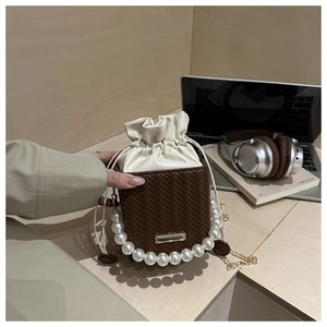 Detail of woven square bucket bag featuring pearl handle and gold chain strap