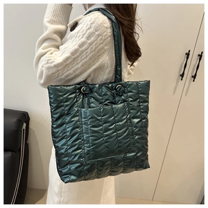 Quilted puffer tote bag in shiny dark green finish shown on shoulder in a lifestyle setting