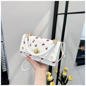 Detail view of a white cherry print crossbody bag with golden flower clasp and woven handle