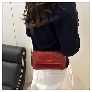 Close-up of wine red patent leather crossbody bag with gold logo on model's shoulder